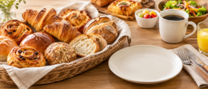複数種類の焼きたてパン、無地の皿、飲み物、カトラリーを配置したランチ準備の静物