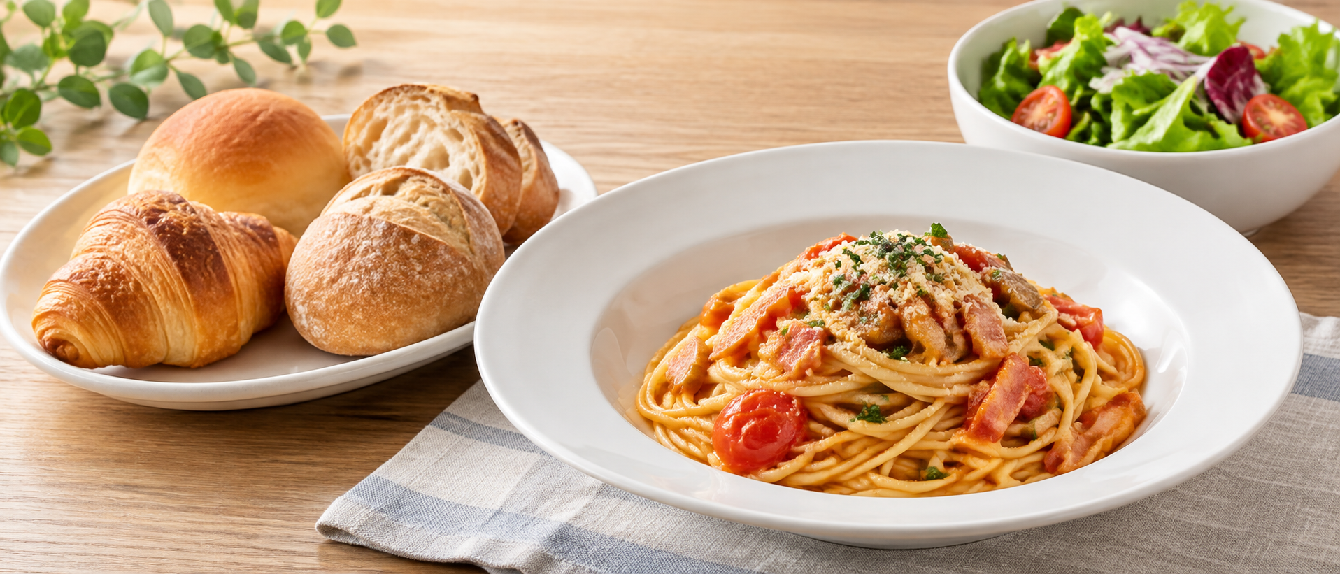 一般的なパスタ、複数種類のパン、サラダを無地の器に配置したランチの静物
